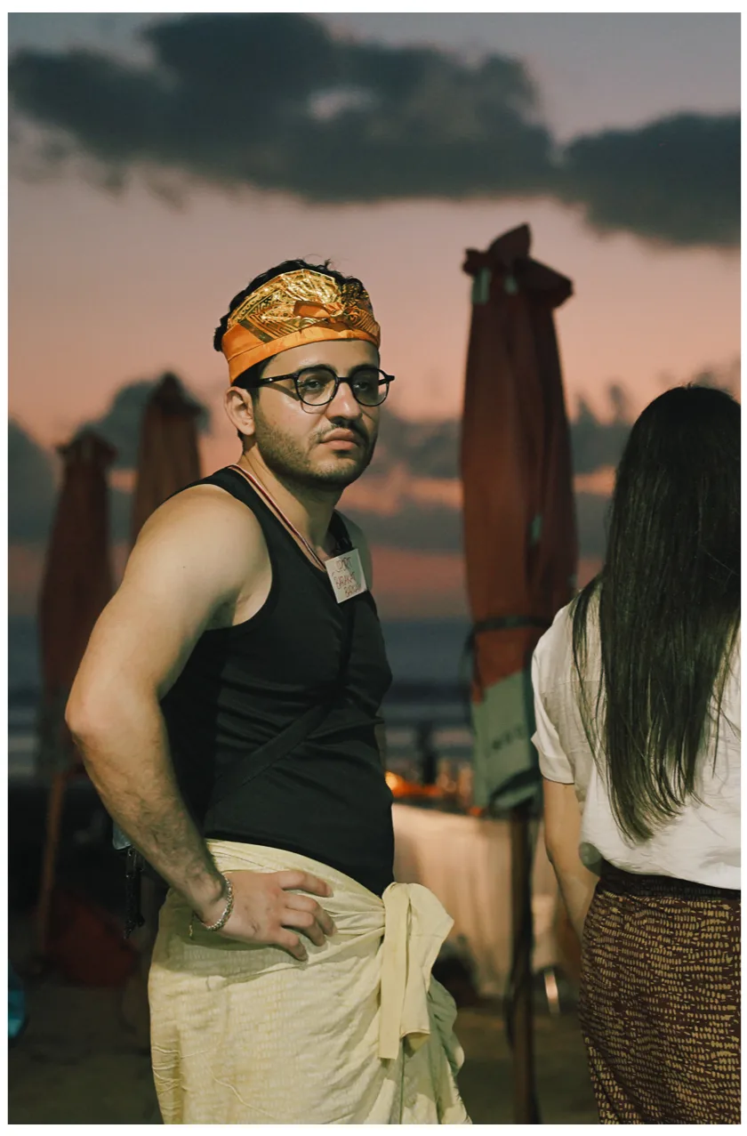 A student in an orange headband and glasses standing on the beach at sunset